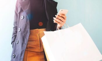 A woman holding a cell phone and bags in her hands as she shops.