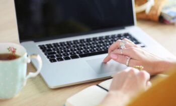 A freelance writer working from a home office desk, using a laptop and drinking coffee.