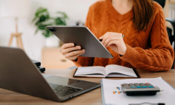 A woman wearing a sweater working on her tablet in her home office for her remote banking job