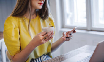 A woman wearing glasses drinking coffee earning free gift cards on her phone