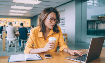 A woman wearing glasses sitting in a coffee shop taking a free online course on her laptop