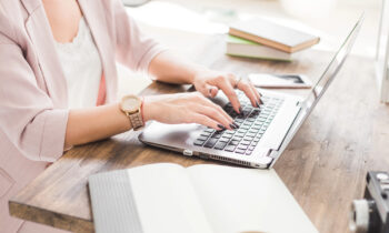 A woman with painted finger nails working on her laptop trying to figure out how to make an extra $2,000 a month