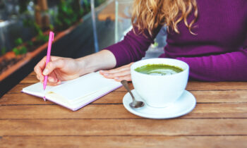 A woman writing in a notebook drinking a matcha latte for blog post paid writing gigs
