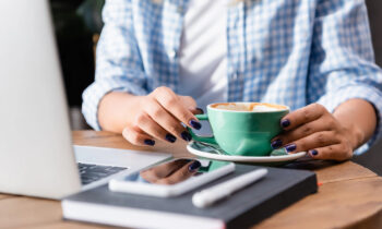 A young woman in a cafe drinking a latte and using her laptop to search for remote jobs that pay $20 per hour