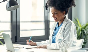 A remote medical scribe working on a laptop and taking notes.