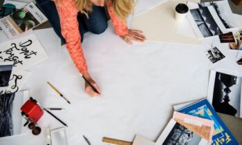 A woman working on a career vision board on the floor, drawing on a large posterboard, with magazine cuttings and collage items in the background.