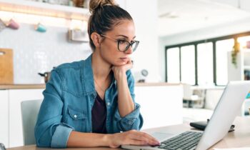 A woman sitting a kitchen table, using a laptop to search for jobs online.